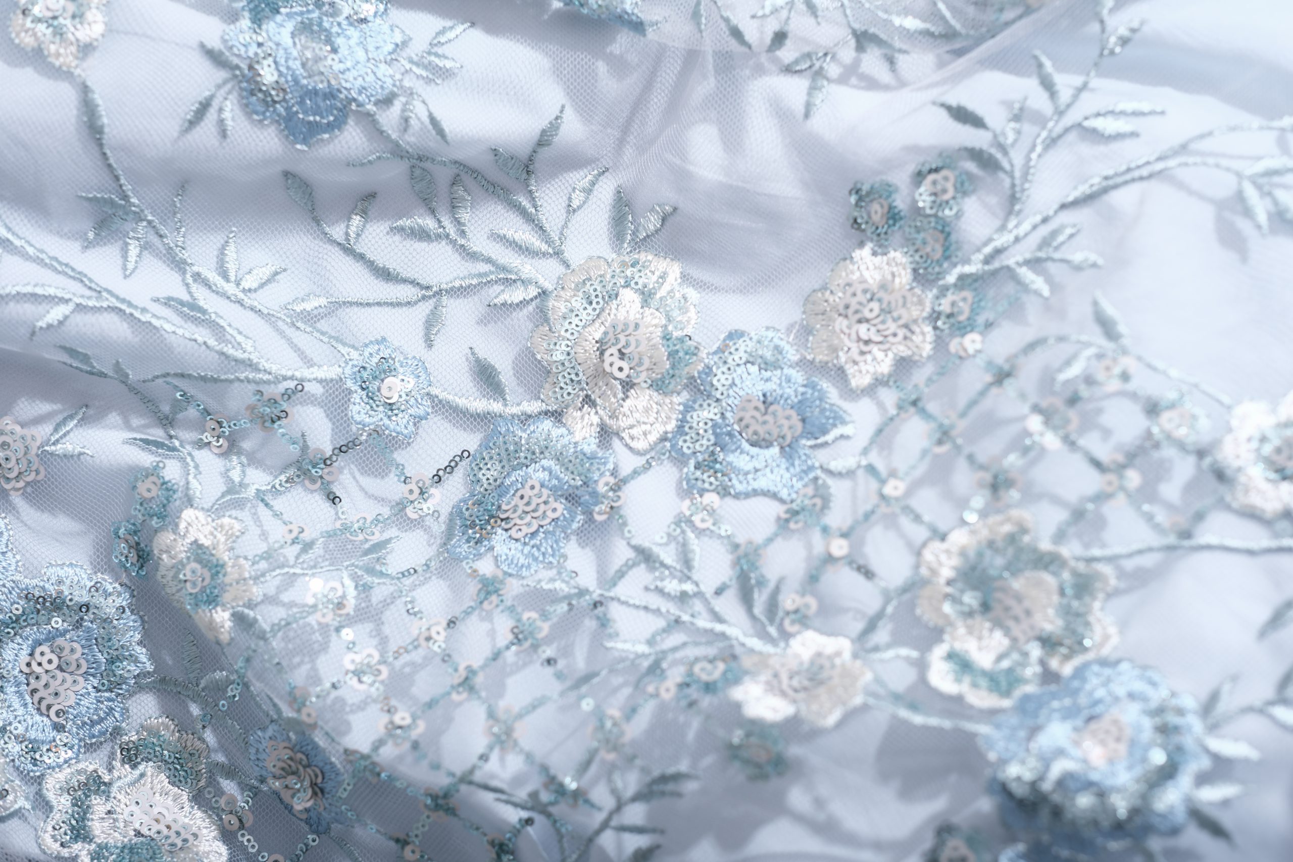 Light blue floral embroidery on delicate fabric used for Bella Krystal’s custom-made gowns.
